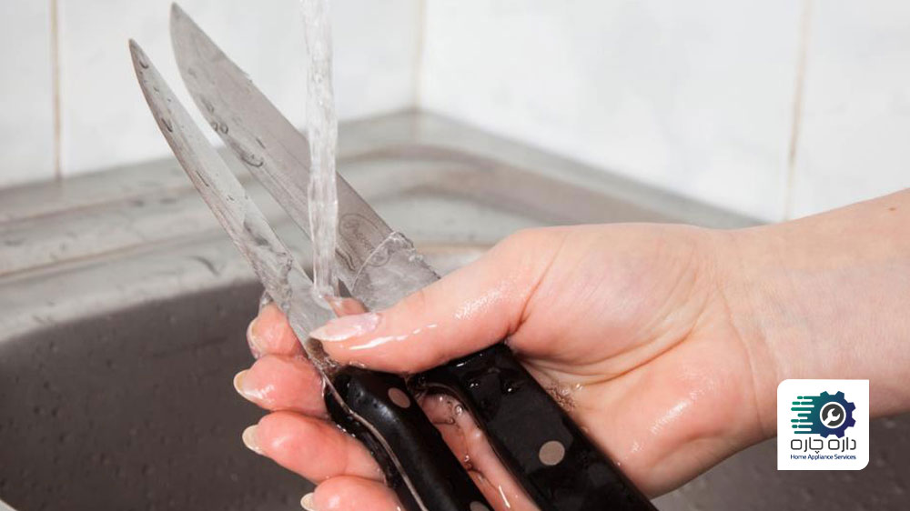 یک نفر که در حال شستن دو چاقو با دست در سینک ظرفشویی