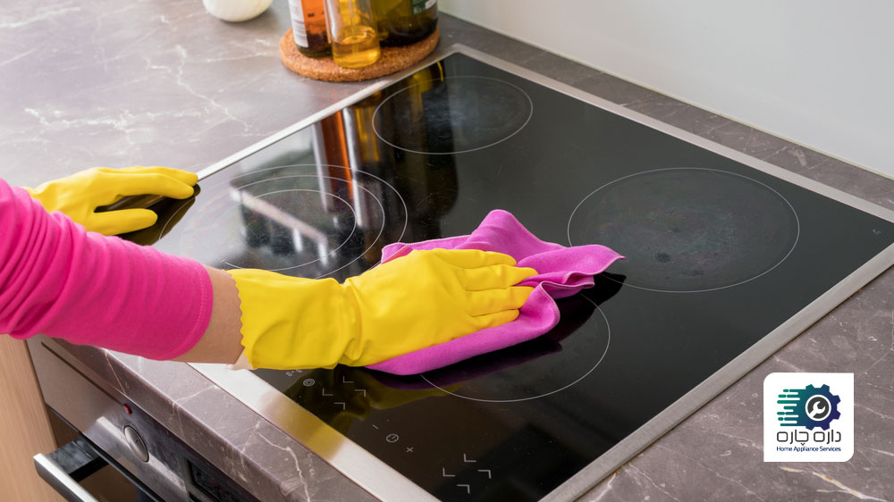 یک نفر دستکش به دست در حال برق انداختن سطح شیشه ای اجاق گاز با دستمال میکروفایبر