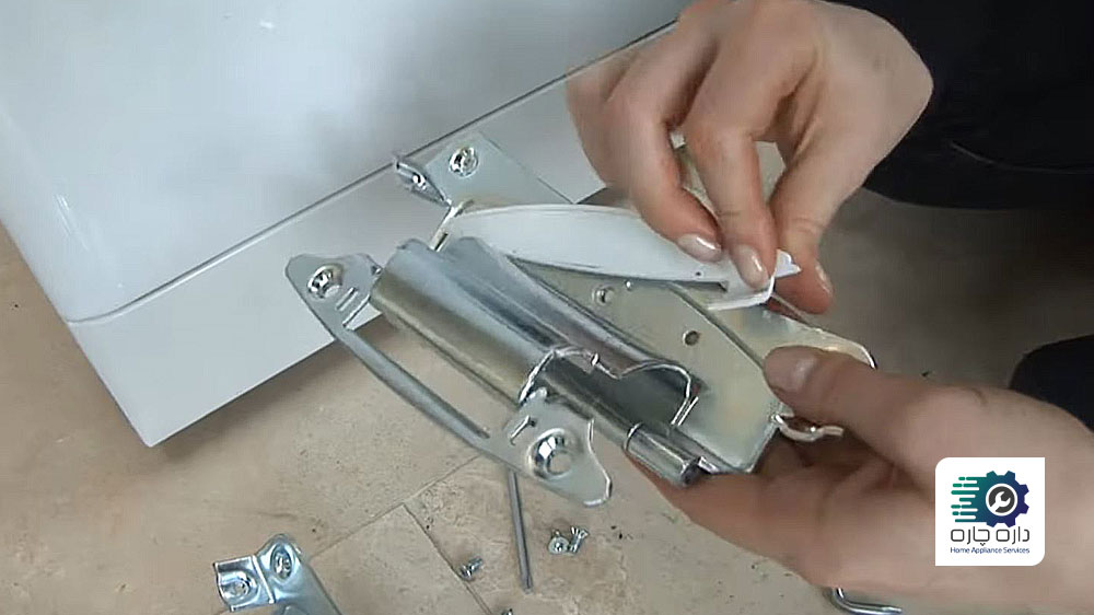 شخصی در حال نصب صفحه پوشش روی لولای جدید درب ماشین لباسشویی آاگ