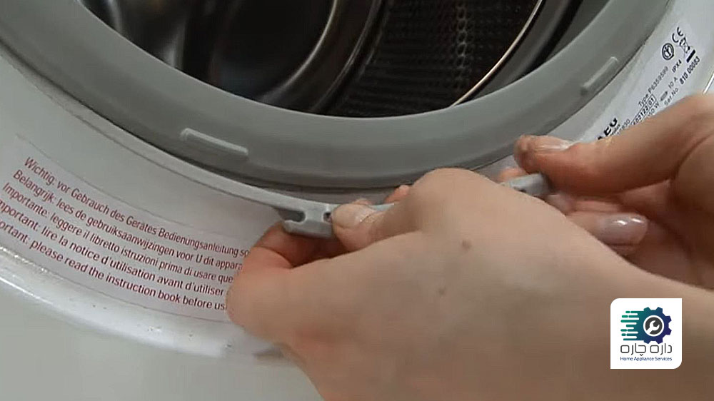 شخصی در حال برداشتن حلقه نگهدارنده لاستیک درب ماشین لباسشویی آاگ