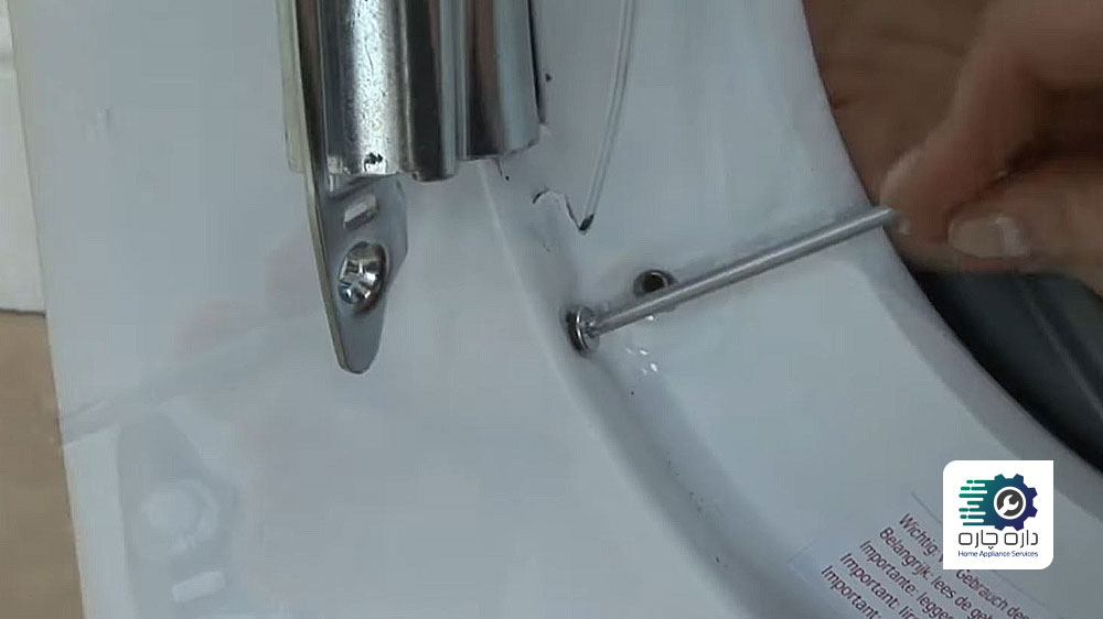 شخصی در حال باز کردن پیچ های لولای درب ماشین لباسشویی آاگ