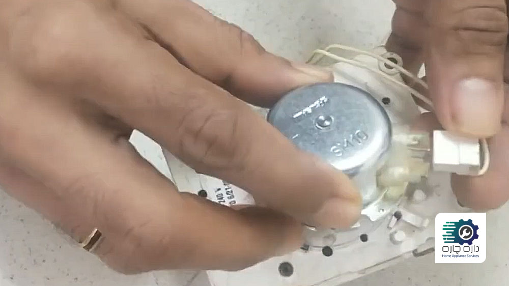 شخصی در حال وصل کردن کانکتور به موتور تایمر جدید ماشین لباسشویی