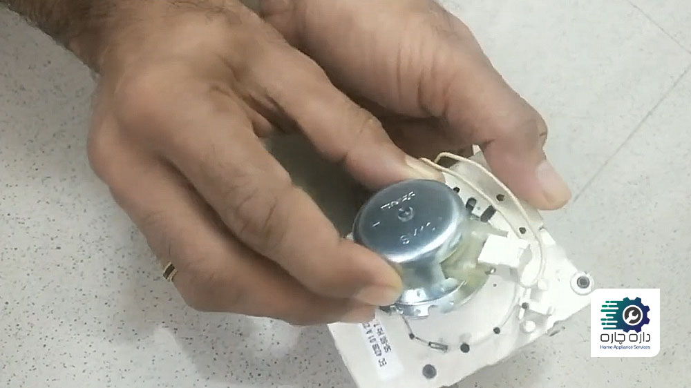 شخصی در حال بیرون آوردن موتور تایمر ماشین لباسشویی